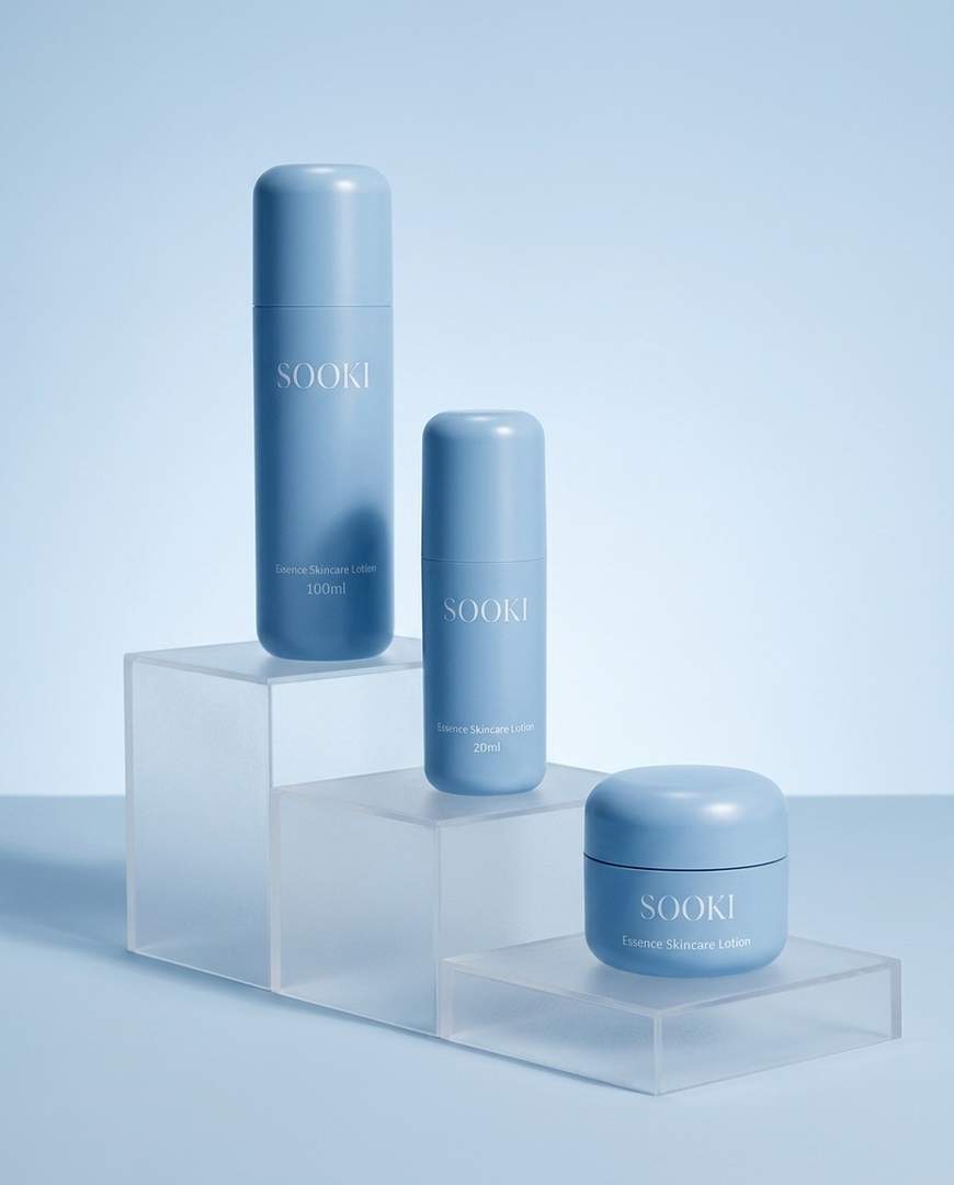 Three frosted pale blue Sooki bottles and a jar arranged on a stone slab